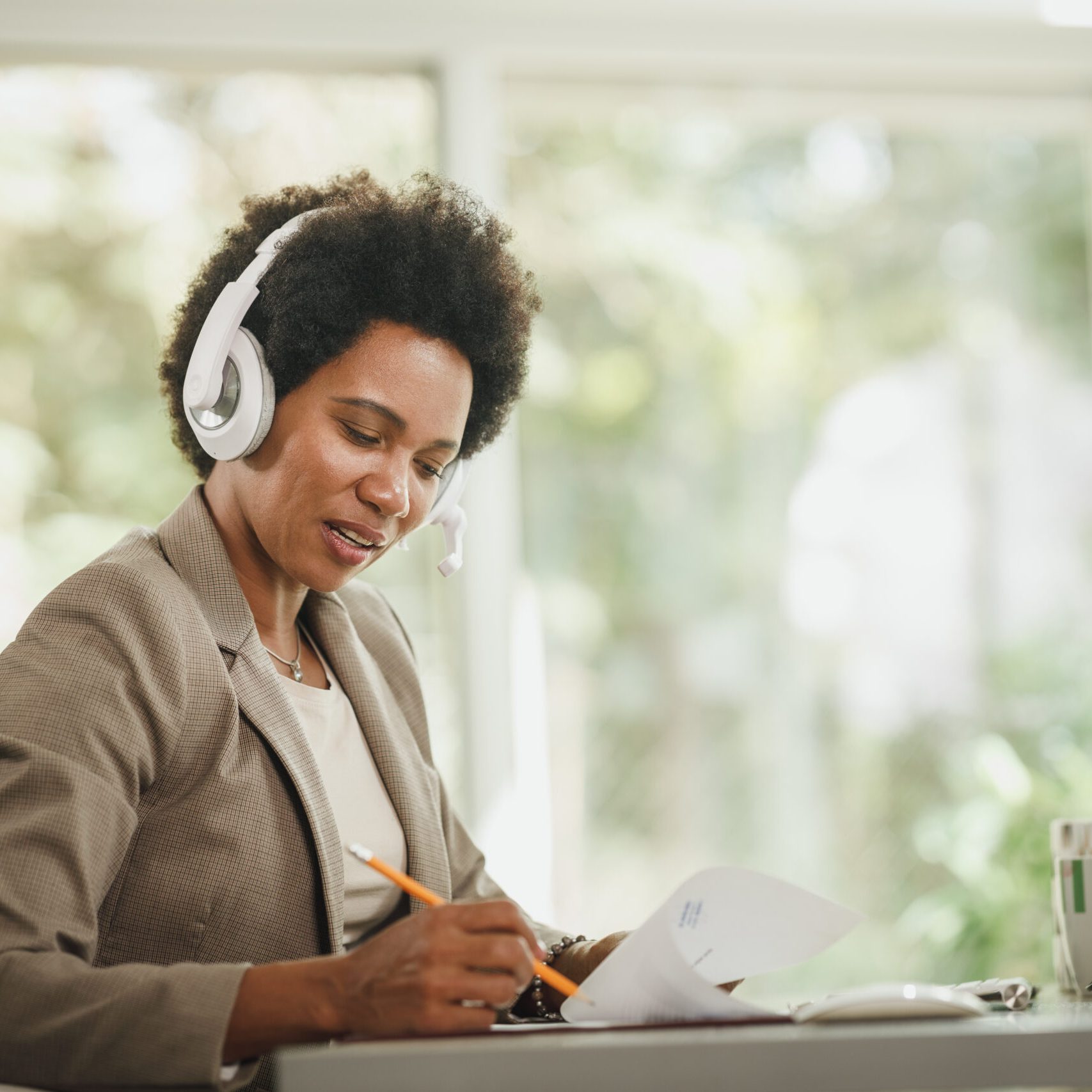 Shot of an African woman wearing a headphones and working at her desk during corona virus pandemic.
